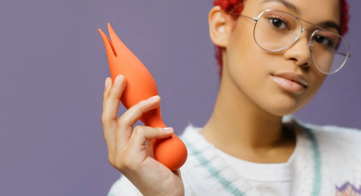A young woman with short red hair holds a modern, vibrant orange object.