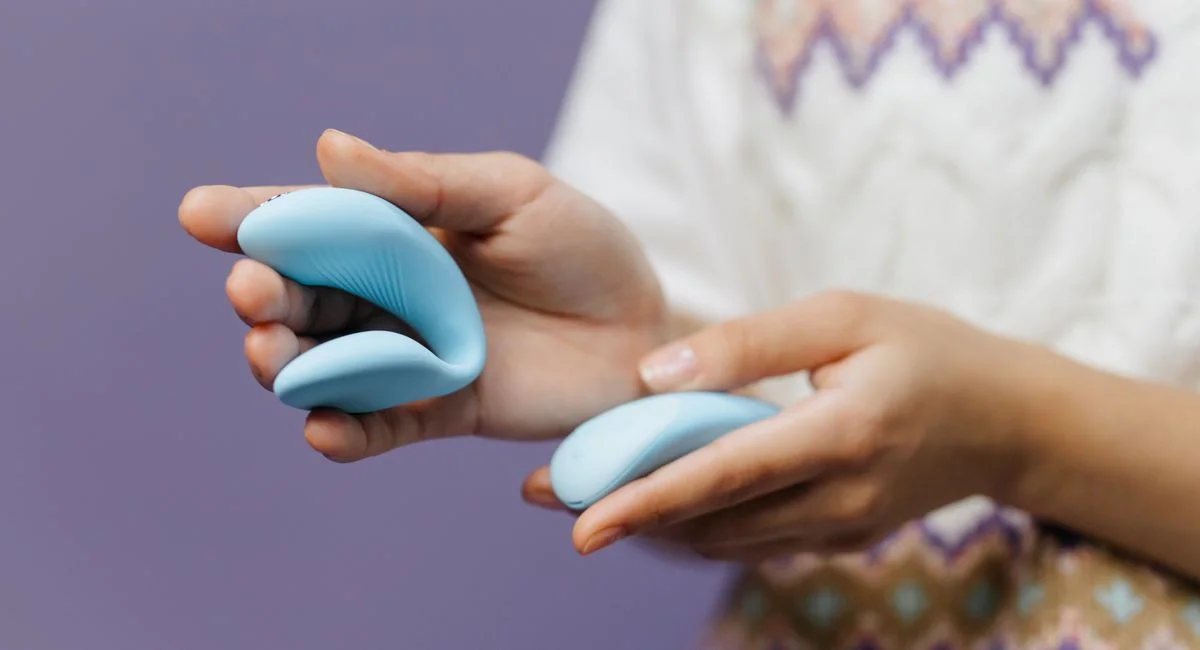 Intimate close-up of hands holding a sleek blue vibrator against a purple background.