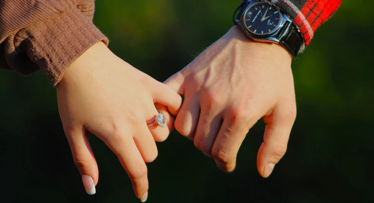 Romantic close-up of a couple holding hands, showcasing an elegant engagement ring.