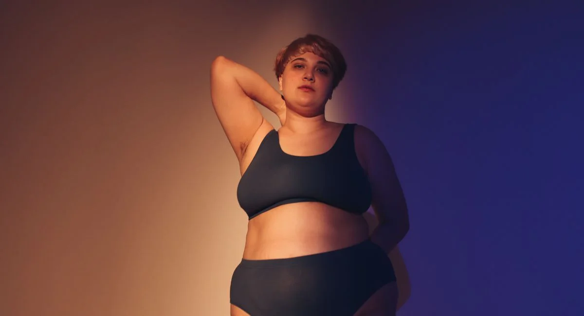 Confident plus size woman embraces body positivity in a studio setting with artistic lighting.