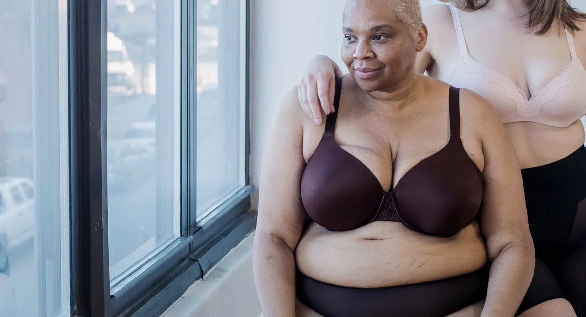 Crop plus size female and overweight African American woman in lingerie spending time together in light room near big window
